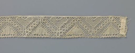 Strip of bobbin lace with heart-shaped and triangular flower between zigzag line of small circles