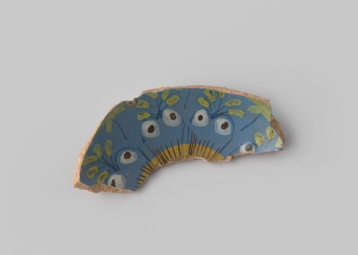 Fragment of a dish, decorated with a floral design in yellow, green, white and black on a blue background