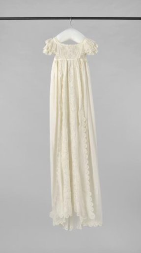 A baptismal dress of white netting with short sleeves. Bodice with embroidered front piece. On the front panel of the skirt plumetis embroidered with fillings of needle lace.