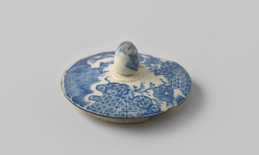 Lid of white-firing earthenware, with a printed decoration of flowers in blue on the upper side, damaged