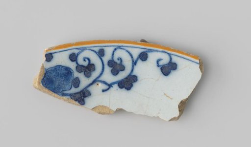 Fragment of white-firing earthenware, with a painting of flower shapes in blue on a white ground on the upper side, with an orange border