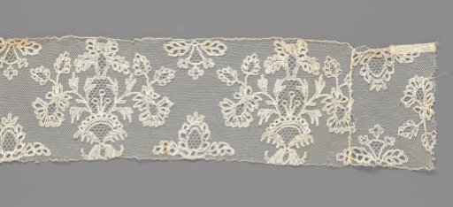 Border of bobbin lace with plume flowers and fan flowers in a conical flowerpot