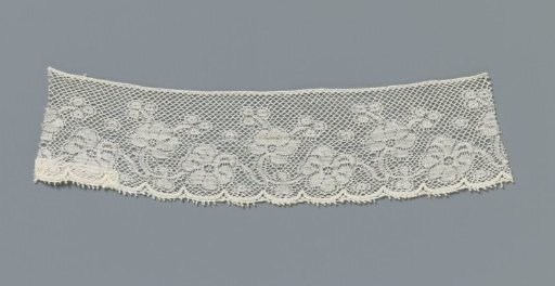 Strip of machine-made lace with a wavy vine with two different flowers and berries