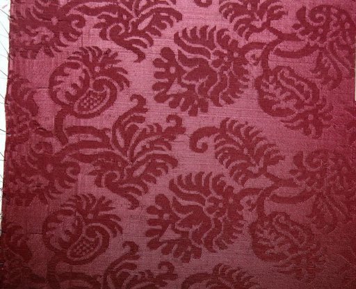 Fragment of red silk damask with a pattern of S-shaped leafy branches with flowers and seed pods