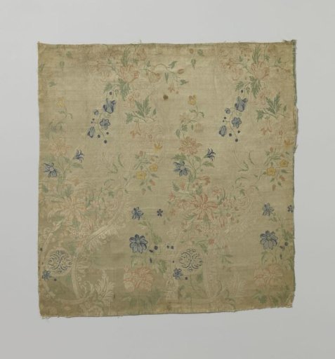 Fragment of multicolored silk with a pattern of scrollwork and stylized leaf motifs on a white ground (brownish discoloration?) with flowers and flower branches in and on the winding bands
