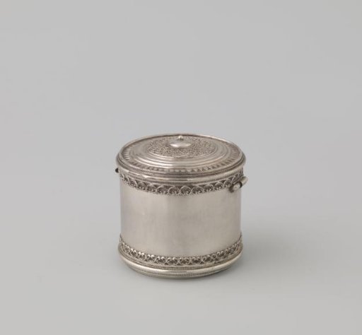 Pyxis, cylindrical with flat lid, chased with lily motifs. Rim of lid and base decorated with openwork fleurons