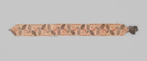 Garter of beige silk with a lance effect; the garter is decorated with flowers and leaves in silver and orange; with silver torsade
