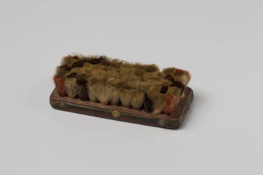 Brush for household use, with a leather-covered back and soft yellow, black, and red bristles
