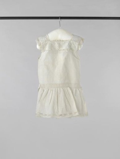 Sleeveless children's smock of white cotton, embroidered with floral and leafy scrolls at the top, and trimmed with lace edging and insertions; fastened at the back with two buttons and a ribbon sash