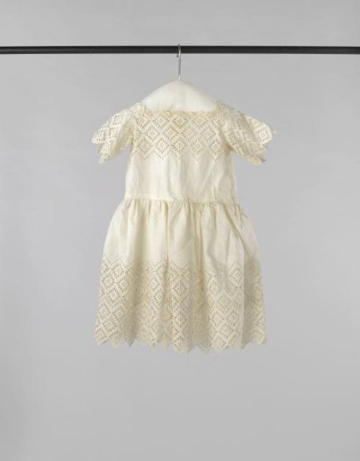 Children's dress of white cotton, with short sleeves of English embroidery and the upper part of the bodice and much of the skirt also embroidered in English style; fastened at the back with eight mother-of-pearl buttons