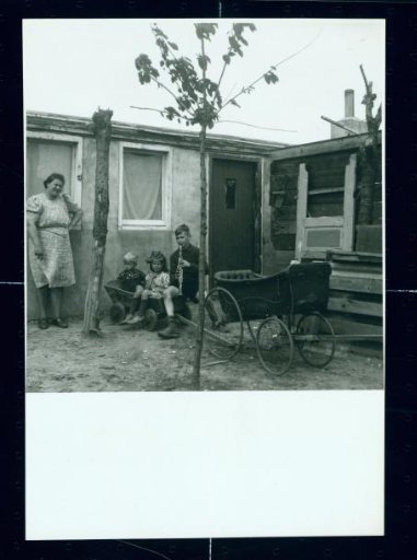 Mother and Three Children by a Dilapidated House