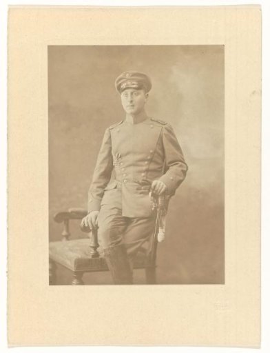 Arthur Moos with a sabre in the uniform of the German Army, with the Iron Cross on his chest, seated on a chair back, December 1914
