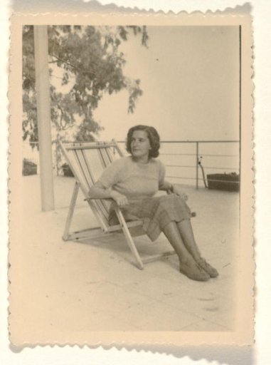 Isabel Wachenheimer seated in a striped deck chair, with a railing and a tree in the background