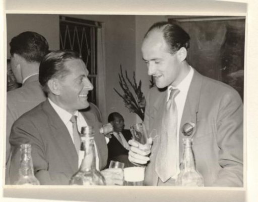 Gideon Elon with a rose in his lapel, smiling in conversation with an unknown man, during a reception during Isabel Wachenheimer's time with KLM