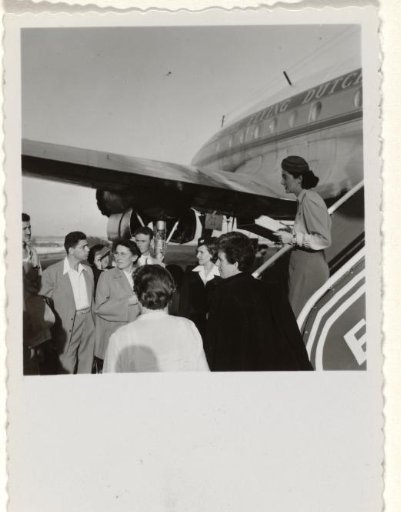 Isabel Wachenheimer standing on the stairs of the KLM aircraft The Flying Dutchman with ground staff and passengers, with the shadow of the photographer on the shirt of the woman in the foreground