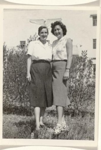 Isabel Wachenheimer with an unknown woman, standing in a grassy field with a hedge in front of a building with a sculpted eagle on the front