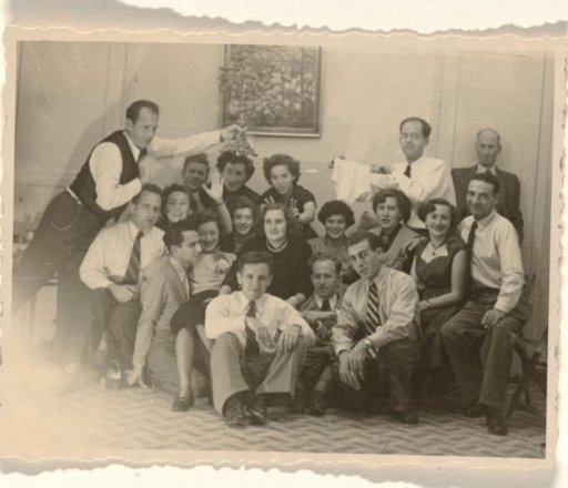 Group portrait of 17 unknown people, Isabel Wachenheimer and Leo Blumensohn, seated on a checkered floor and in front of a painting with a floral design