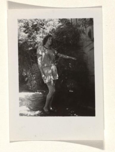 Isabel Wachenheimer in a striped top and shorts, with her knees bent and her left arm resting on a shrub