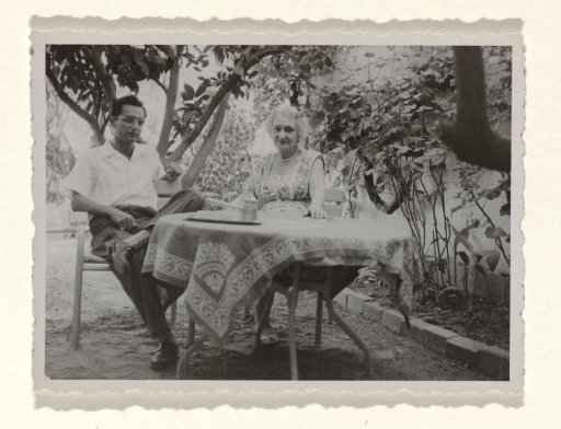 Karl-Heinz Arndtheim, the second husband of Isabel Wachenheimer, and an unknown woman, seated at a table covered with a patterned cloth, outdoors, in front of a vegetated wall
