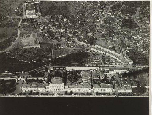 Aerial photograph in black and white of a town or village situated on the water, with a long U-shaped row of buildings