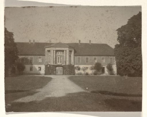 Front view of a country house with a pavilion-like central section, with trees on either side and a lawn and driveway at the front