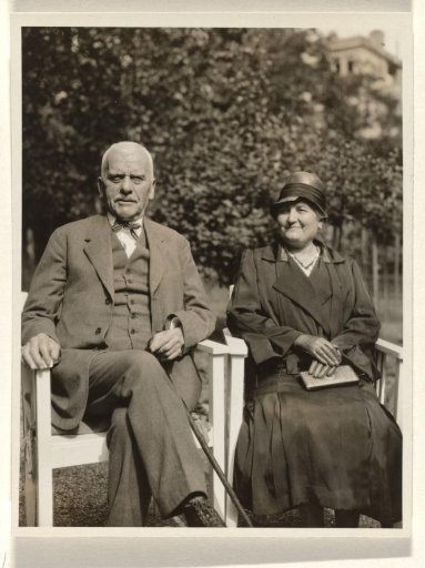 Meir Wachenheimer with a cane in his hands and his wife Mathilde Wertheimer-Wachenheimer with her hands folded over a portfolio on her lap, seated on chairs in a garden