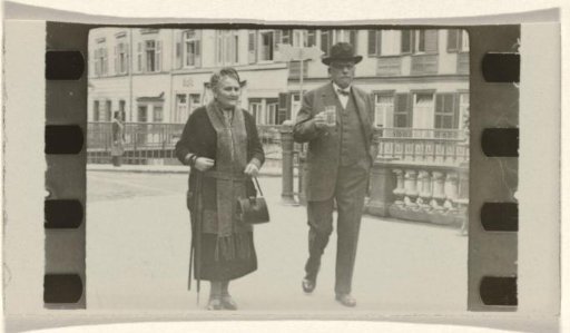 Meir Wachenheimer with a glass in his hand and his wife Mathilde Wachenheimer-Wertheimer with an umbrella on her arm and a bag in her hand, walking along a street