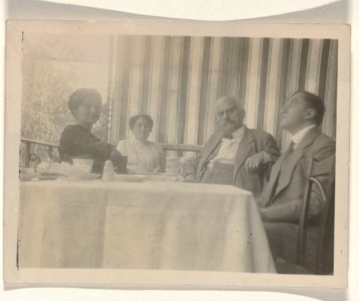 An unknown woman, Mathilde Wachenheimer-Wertheimer, Meir Wachenheimer, and Eugen Wachenheimer seated at a set table with a tablecloth, with a wall featuring striped wallpaper in the background
