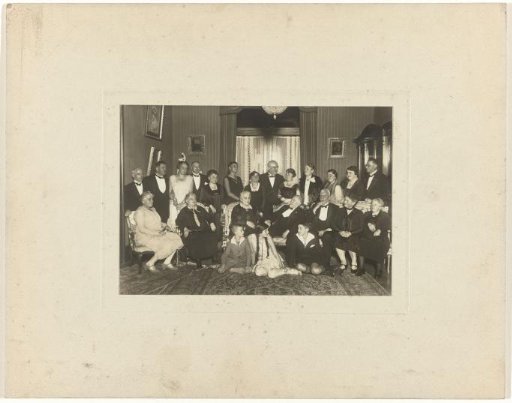 Meir Wachenheimer and Mathilde Wachenheimer-Wertheimer at a festive event in a hall with unknown people, with a carpet on the floor, doors in the background, and paintings on the side and back walls