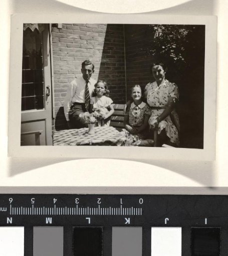 Four unknown persons, seated outdoors with a stone wall in the background and a checkered tablecloth in the foreground