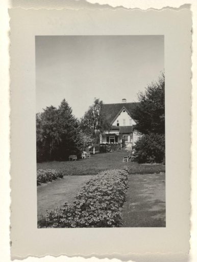 House Fahrenkamp, viewed from a distance, with a lawn, a shrub hedge and trees in the foreground