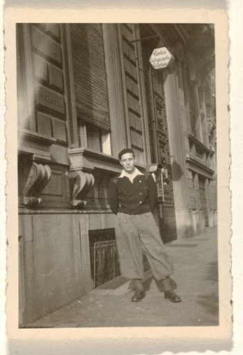 Unknown man in breeches, with a flat cap and shirt protruding above his outer garment, standing on the street