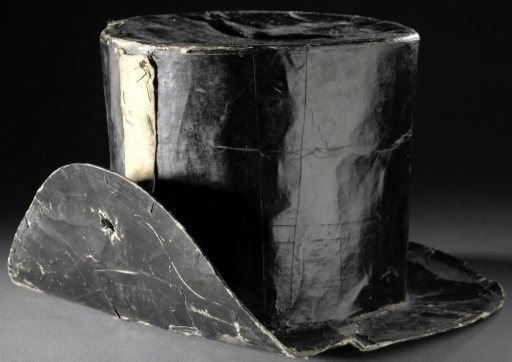 Hat of black glossy paper over a cardboard core with a wax-cloth lining, with a straight crown and narrow, straight brim folded up on one side, so-called paper hat