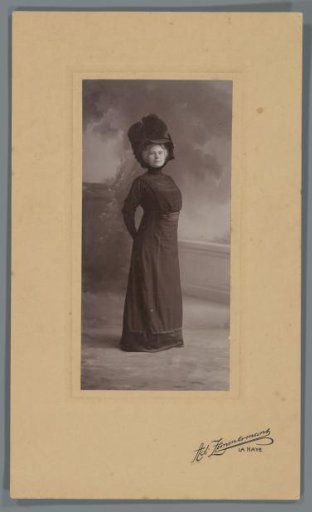 Standing studio portrait of Jeannette Bouman-De Lange in dark clothing with a large hat