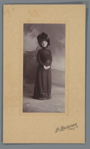 Standing studio portrait of Jeannette Bouman-De Lange in dark clothing with a large hat