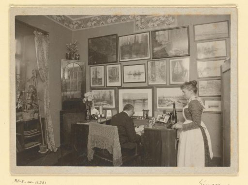 Franz Rieffel seated at a desk, surrounded by his art collection, together with his caretaker Marie