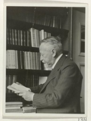 Andries Bonger, standing by a bookcase, a book in his hands