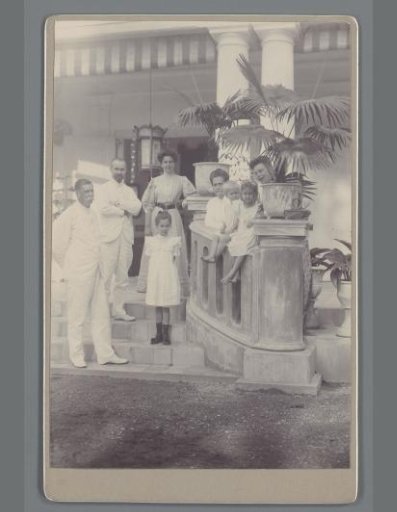 Group portrait of unknown men, women and children on the steps of a veranda
