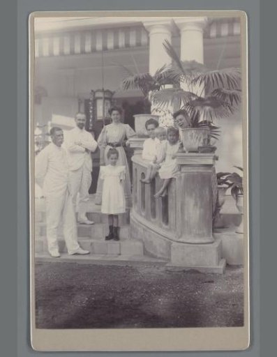 Group portrait of unknown men, women and children on the steps of a veranda