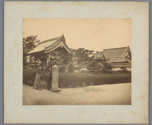 Sandy path with buildings and a Buddha statue in the background (possibly) in Japan
