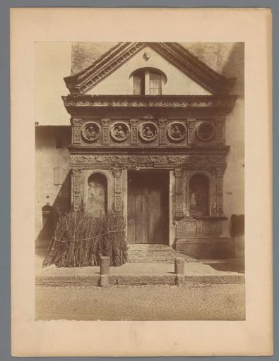 Facade of a building with bunches of branches in front, presumably in Italy