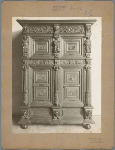 Cabinet with lower and upper sections, closed by four doors, between fluted pilasters, decorated with carved work of presumably religious scenes