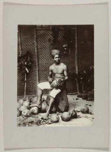 Studio portrait of a boy with coconuts in the Dutch East Indies