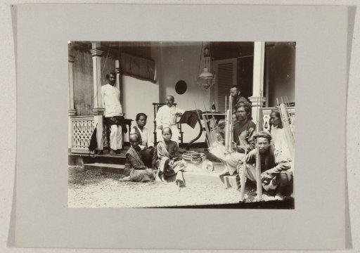Two European men on a veranda, surrounded by Indonesian people