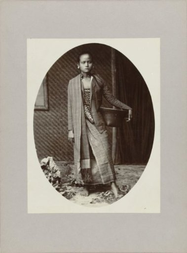 Studio portrait of a girl with a basket on her hip in the Dutch East Indies