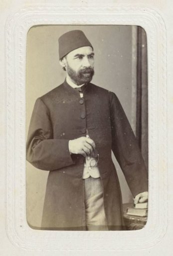 Studio portrait of a man in a long coat with a fez on his head