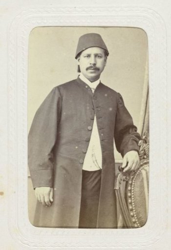 Studio portrait of a man with mustache in a long coat with a fez on his head