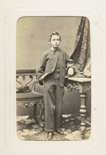 Studio portrait of a boy in a three-piece suit next to a table