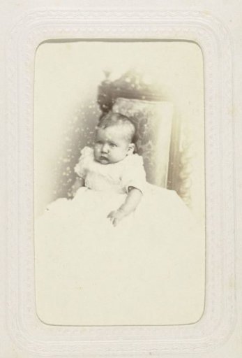 Studio portrait of a baby in a white dress on a chair
