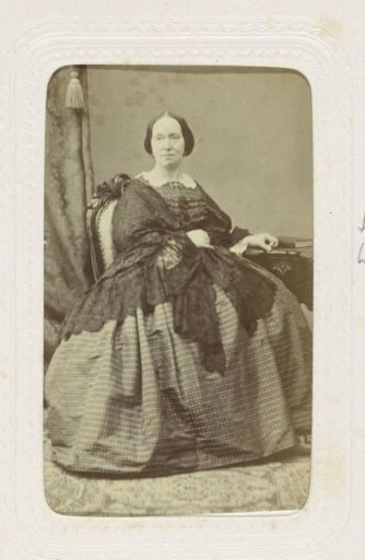 Studio portrait of a woman in a full dress, seated at a dressing table